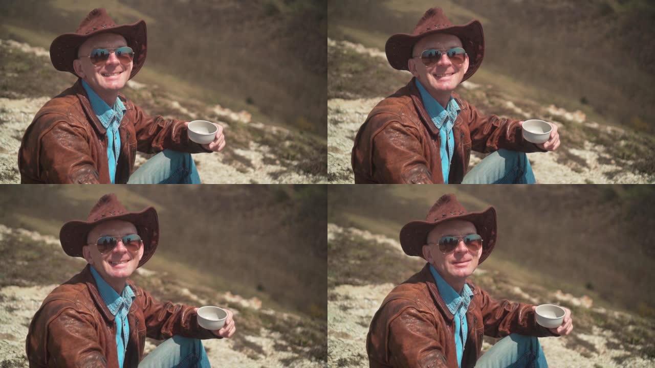 在山上，一个男人戴着牛仔帽，皮夹克，蓝色牛仔裤和眼镜。男人看着镜框笑了。