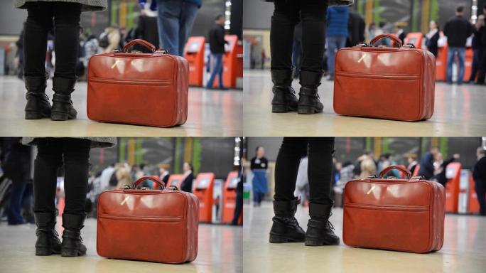 在机场，穿着靴子和红色手提袋的女人，还有一些散焦的人。我们只看到腿和红色袋子。
