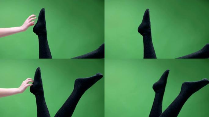穿着可爱的黑色针织膝袜的女性青少年腿的特写镜头，嬉戏地移动，背景孤立在绿色上。有趣的女孩摩擦和抓挠她