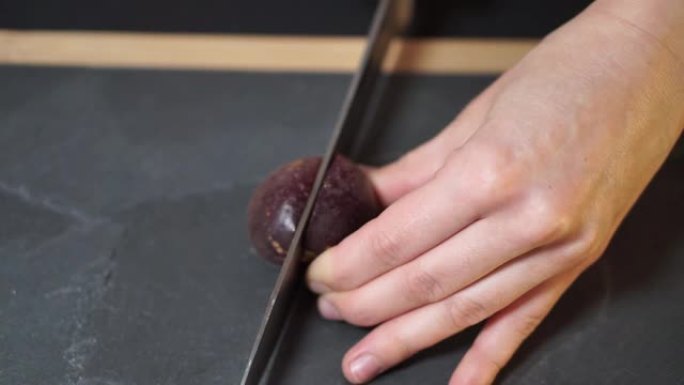 特写镜头，一个女人的手拿着一把刀，把百香果切成两半，然后把两半拿到摄像机上，然后用木框放在厨房的石板