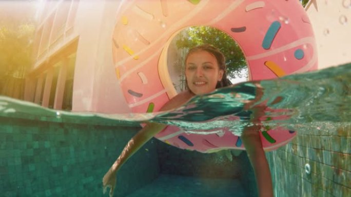 年轻的时髦千禧一代女孩在游泳池里撒满甜甜圈，微笑着看着相机。阳光明媚的日子，年轻快乐的女人在蓝色游泳