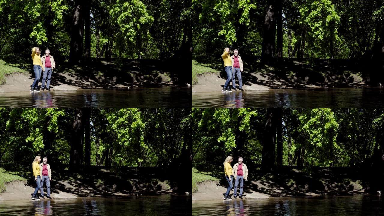 充满爱心的高级夫妇站在树林的湖边，看着风景愉快地交谈。快乐成熟的恋人在大自然中有浪漫的户外约会