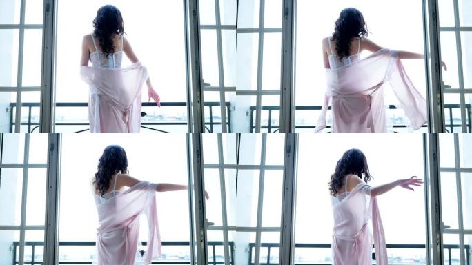 穿着粉色丝绸长袍的性感女孩站在阳台上跳舞