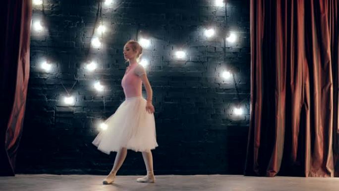 美丽的芭蕾舞女演员在pointe上旋转着自己。黑暗的工作室背景。