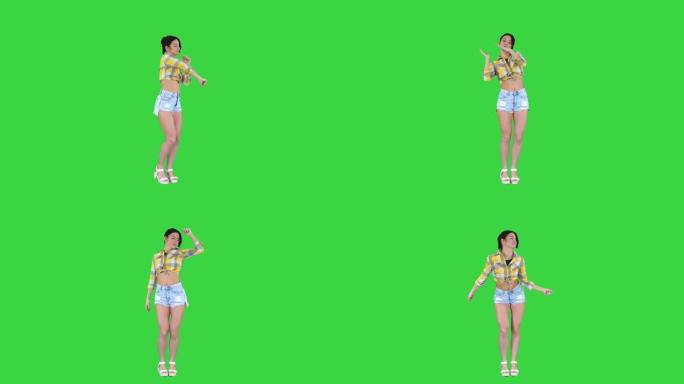 穿着方形衬衫和牛仔裤短裤、运动鞋、在绿色屏幕上跳舞、色键的女孩