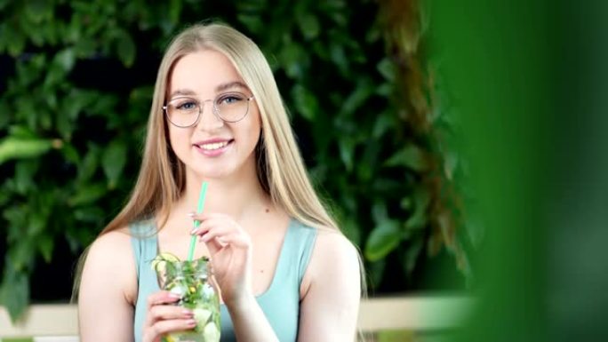 微笑的年轻女子的肖像坐在森林的长凳上，与新鲜的排毒鸡尾酒合影