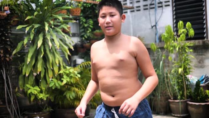 肥胖的青春期男孩在户外后院移动和摇晃他的肚子，慢动作。