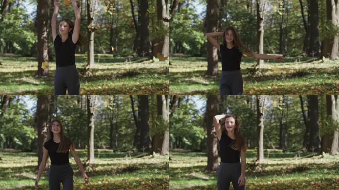 女孩在秋天的公园里遮住脸，挥舞着枫树树枝，树枝上有黄色的叶子。慢动作