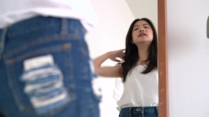 年轻美丽的亚洲女人穿上衣服后看着镜子，为夏天在酒店房间的下一次旅行做好准备。