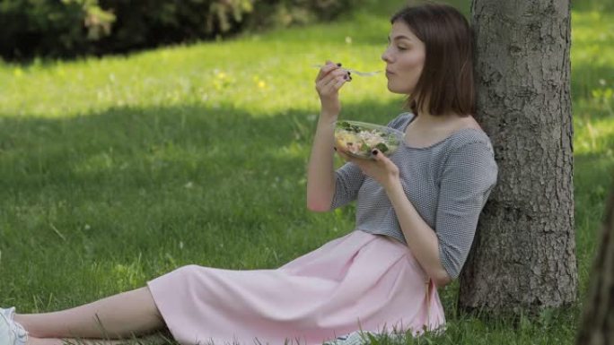 女人坐在夏季公园吃新鲜沙拉