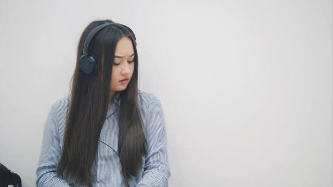 受启发的年轻亚洲女孩坐在耳机的地板上，听音乐，停止写作并自拍。
