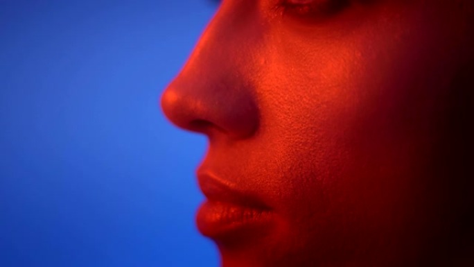 在蓝色背景上的红色霓虹灯中严肃的时装模特的眼睛和嘴唇轮廓的特写镜头。