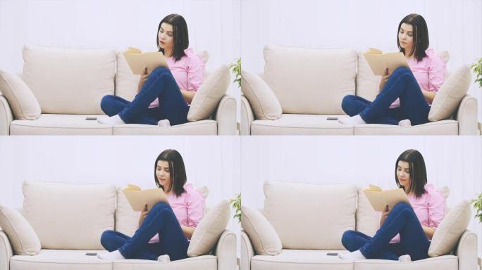 好奇的年轻女子正坐在沙发上，以莲花的姿势，阅读着书，对情节的情感反应。