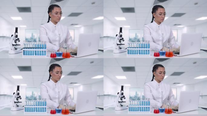 一位女科学家坐在化学实验室的白桌旁，将临床试验数据写入笔记本电脑。