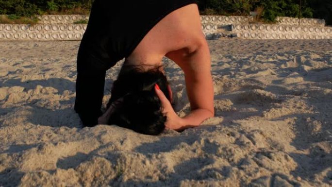 穿着黑色紧身衣的女人在日出时在美丽的海滩上靠海做瑜伽练习。健身、运动、瑜伽和健康生活理念。4k. 4
