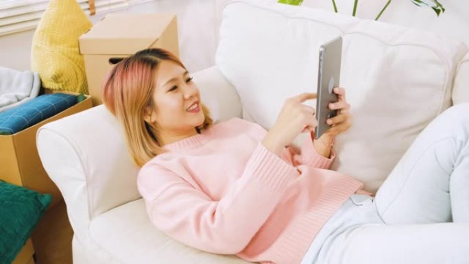 亚洲妇女躺在沙发上，在家中使用平板电脑，情绪低落。数字时代的生活方式。