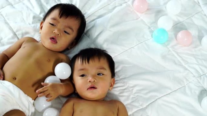 欢快的双胞胎婴儿在床上玩彩球