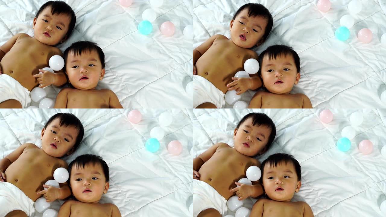 欢快的双胞胎婴儿在床上玩彩球