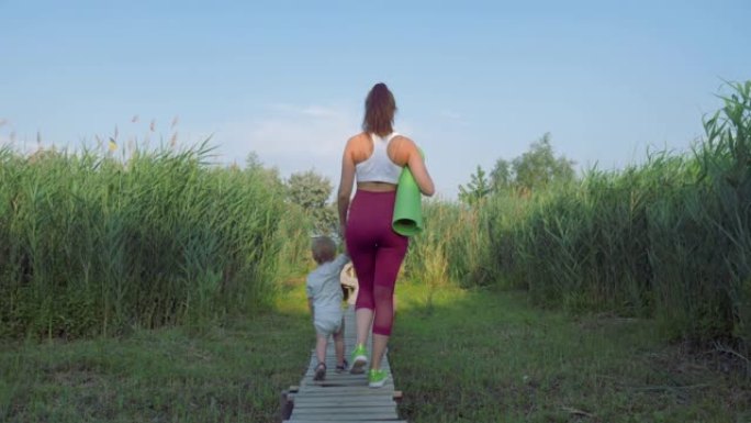 体育家庭，年轻的体育母亲带着小孩在练习健身后走在绿色植被中的桥梁上