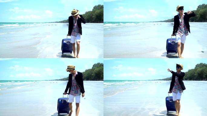 4k景观前视图跟踪拍摄年轻的亚洲商人游客携带蓝色行李，在沙滩上漫步，海浪和岛屿背景。商人在夏季海滩度