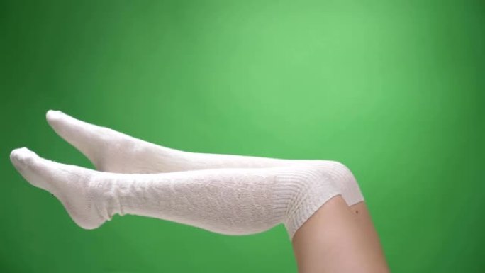 可爱的白色袜子中女性嫩腿的特写镜头诱人地移动，背景孤立在绿色上