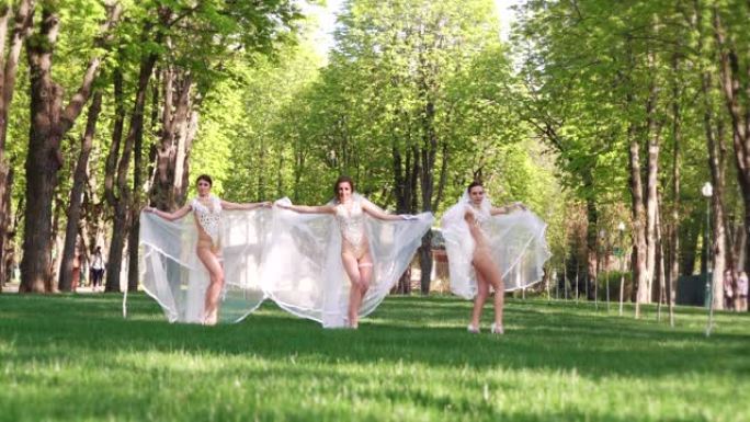穿着性感服装和新娘面纱的女舞者在绿色公园跳舞