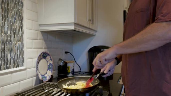 40多岁或50多岁的男人在厨房里用红色的硅胶刮刀争夺鸡蛋