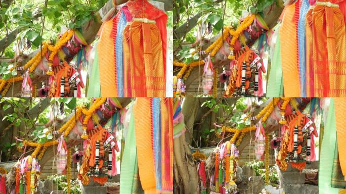 五颜六色的祭坛附近树上的衣服。一堆明亮的传统衣服作为礼物送给悬挂在泛灵论者祭坛附近树枝上的泰国烈酒