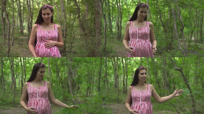 公园里的怀孕女孩在绿树的背景下。一个穿着白色条纹红色连衣裙的女孩穿过公园。