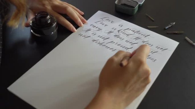 一个年轻女子使用刻字技术在纸上写字的特写镜头。她写了一个婚礼誓言爱是耐心的爱是善良的