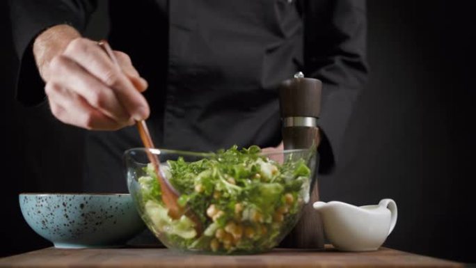 男人将素食绿色沙拉与深色背景上的木勺混合在一起