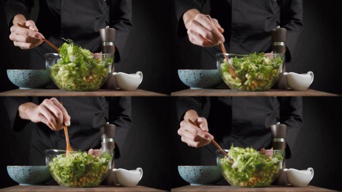 男人将素食绿色沙拉与深色背景上的木勺混合在一起