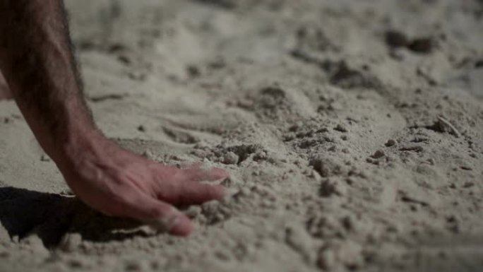 近距离拍摄一名男子触摸沙滩的手。慢动作现实生活
