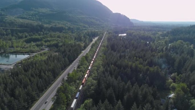 载有集装箱的货物火车在附近山区通过铁路经过视频，火车后的前向摄像机运动。