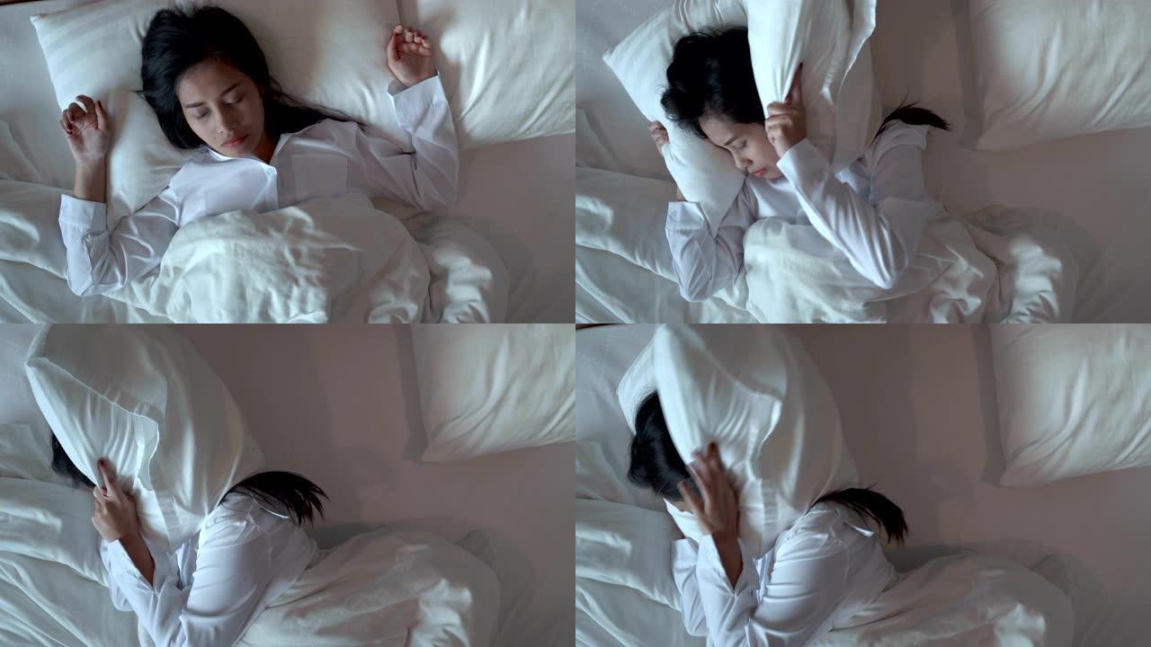亚洲妇女不睡觉，因为打扰噪音，她睡不安稳，把枕头放在她的耳朵上。