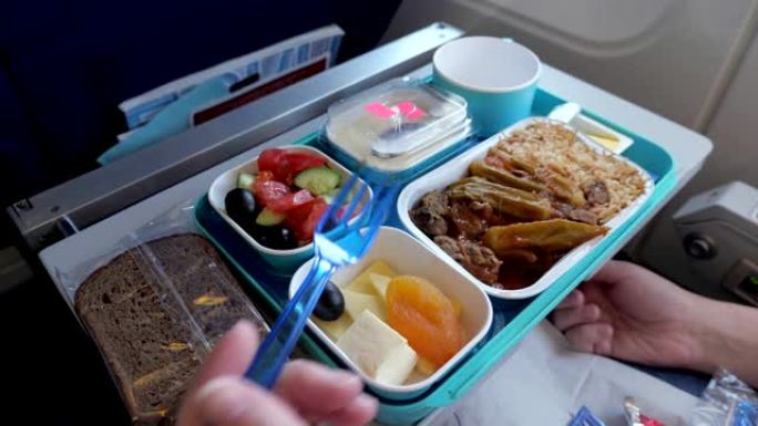 女人在飞行过程中在飞机上吃饭，食物放在托盘上，手特写。