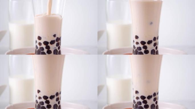 慢动作-将奶茶倒入玻璃杯中，在明亮的大理石桌子和白色托盘上放美味的台湾木薯珍珠泡泡。4k视频拍摄。