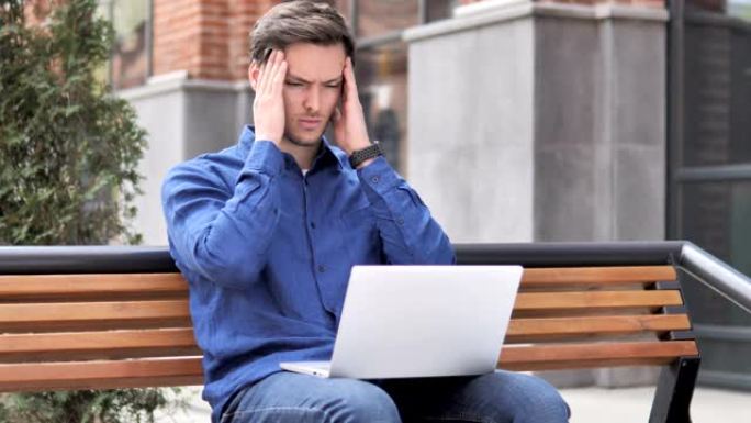 坐在户外头痛的年轻人使用笔记本电脑