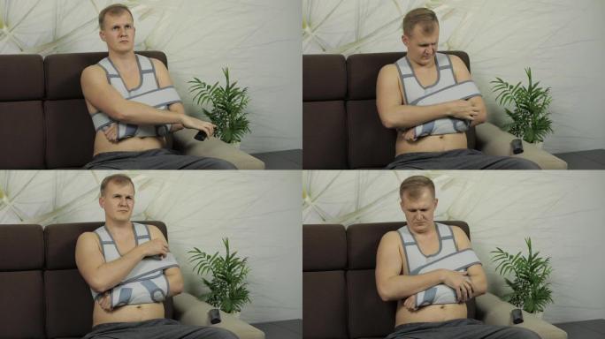 手臂骨折的痛苦男人戴着手臂支撑坐在沙发上看电视