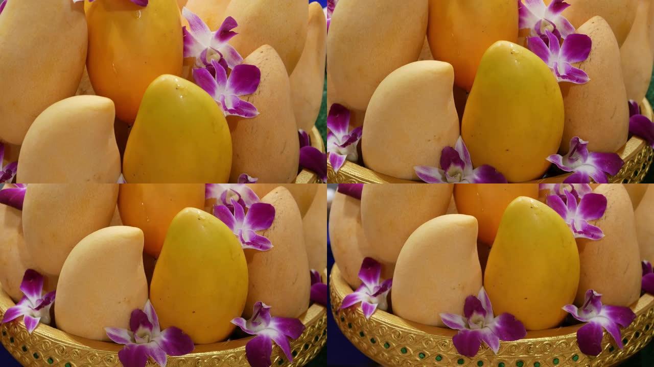 有芒果和鲜花的金盘子。美味成熟的黄色芒果和美丽的紫色兰花花放在闪亮的金色盘子里，作为传统的东方甜点和