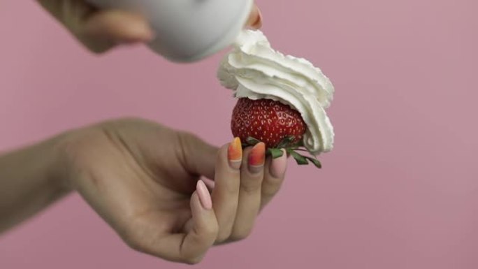 女人握着草莓，在浆果上挤出鲜奶油