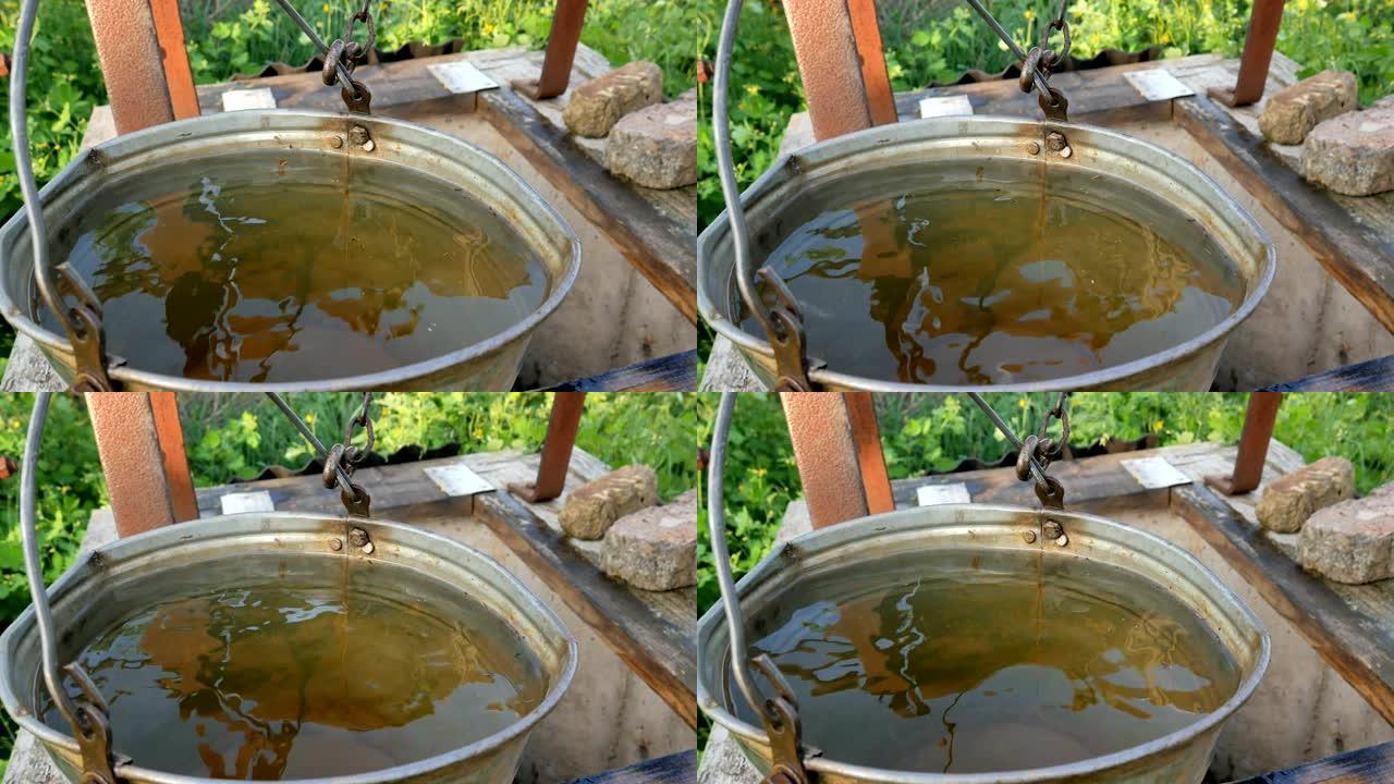 井里的脏水。地球的生态学。女人用水桶把链子扔进乡村井取水。