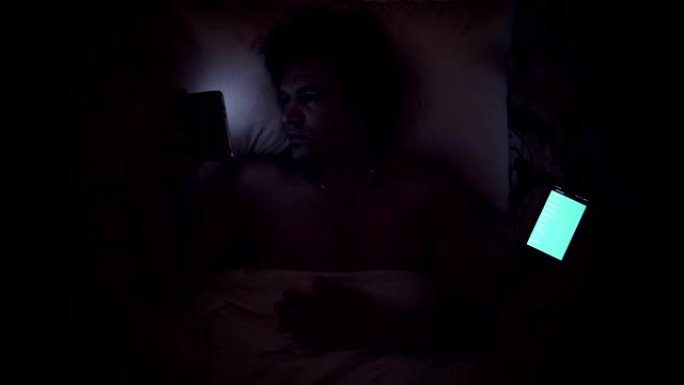 男人在床上用手机看平板电脑。