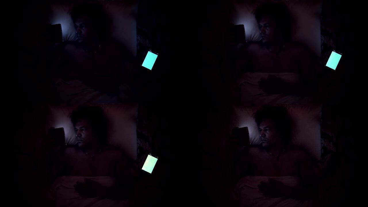 男人在床上用手机看平板电脑。