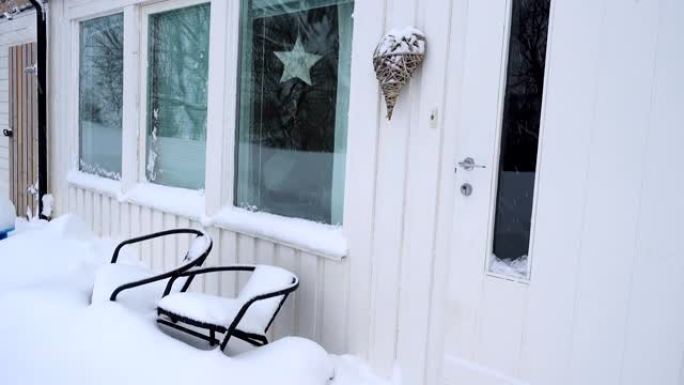 白色木制斯堪的纳维亚房屋的门廊，在大雪期间带有房屋装饰