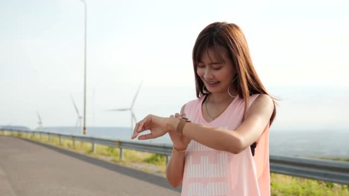 亚洲妇女在清晨在风力涡轮机场慢跑或跑步。健康在跑步时y concept.us智能手表。