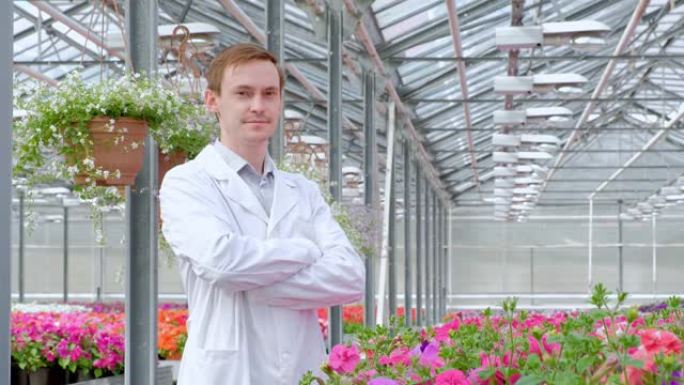 一个穿着白大褂的年轻人，科学家生物学家或农学家检查并分析了温室中的花朵和绿色植物。