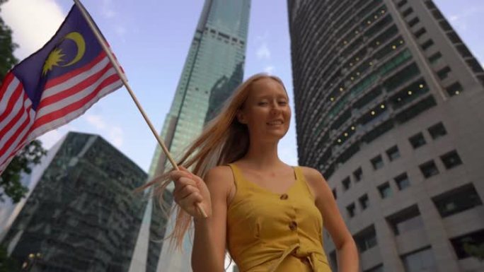 一名年轻女子挥舞着马来西亚国旗的慢镜头，背景是摩天大楼。去马来西亚旅游的概念