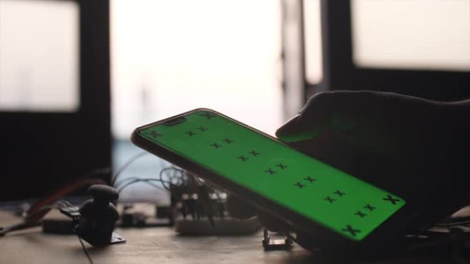 在桌子上拿着和滚动绿色屏幕的智能手机，带DIY电路
