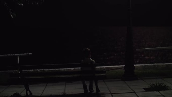 孤独的孩子晚上坐在户外的长凳上